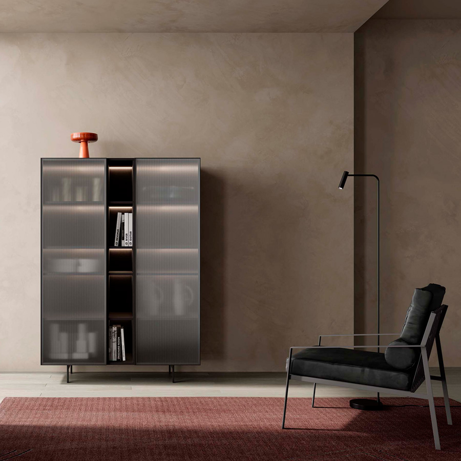 Ambiente con mueble contenedor Sense 08 con puertas con marco de aluminio y cristal estriado, sillón de lectura y lámpara de pie