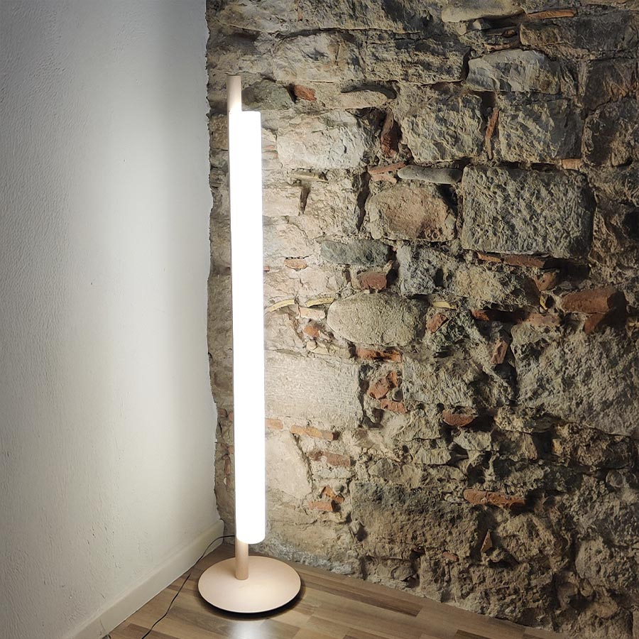 Lámpara de pie Stick con pantalla de lino blanco encendida.