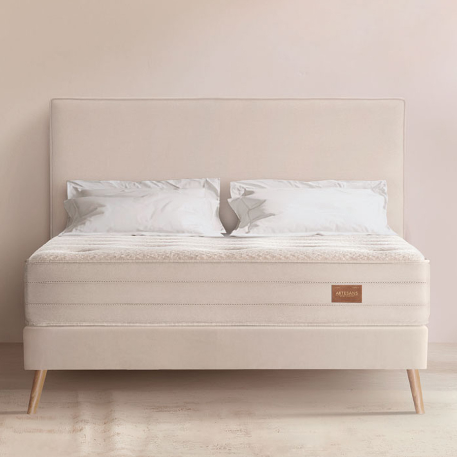 Colchón Artesans sobre cama tapizada color beige con patas cónicas de madera