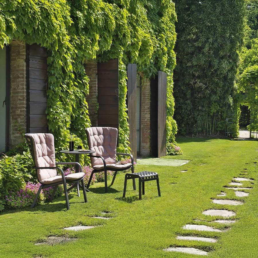 Sillón de terraza Folio confort de Nardi en acabado estructura tortora y cojín rosa, en vista de ambiente de jardín.
