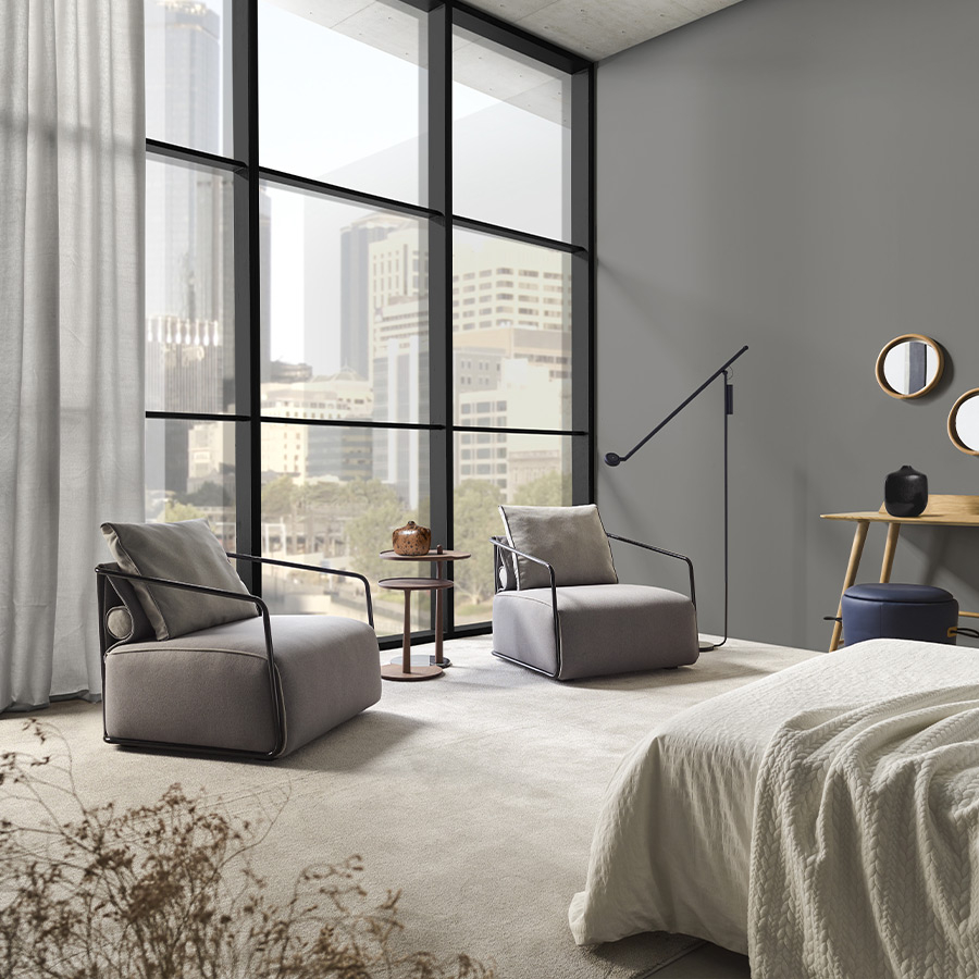 Butaca Adex de la firma Frajumar en vista de ambiente de dormitorio y tapizado gris.