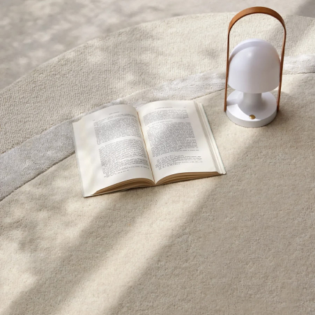 Alfombra Aura confortable de tonos neutros con sombras proyectadas y un libro y lámpara portátil apoyada sobre ella.