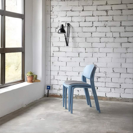Dos sillas del modelo Smart con base tapizada apiladas frente a una ventana en el interior de un edificio estilo industrial.
