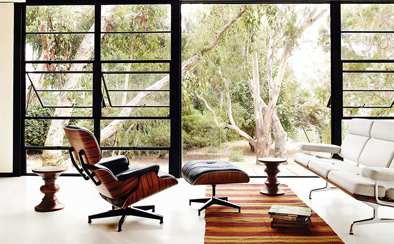 Sillón relax fijo Eames con reposapiés de diseño, cuerpo de madera y tapizado en piel de color negro.