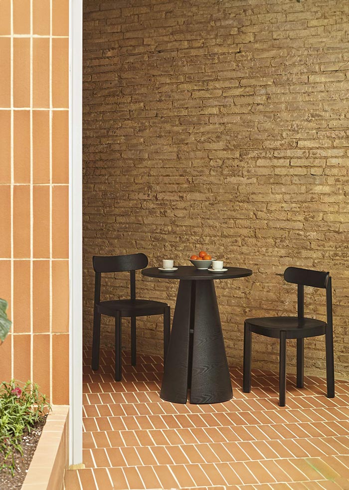 Conjunto de dos sillas Nara y mesa a conjunto de madera oscura en negro en un patio interior.