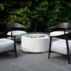 Cuatro butacas Africa de Vondom negras alrededor de una estufa de piedras en un espacio exterior ajardinado