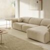 Sofá curvo con reposabrazos redondos tapizado en color crema en un salón con luz natural y tonos arena.