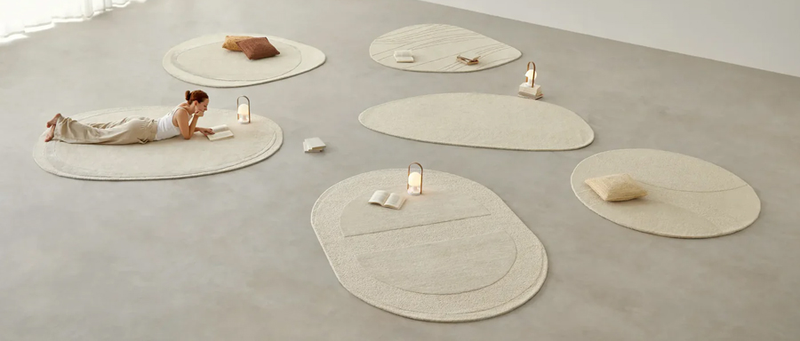 Conjunto de alfombras claras con formas orgánicas pertenecientes a la colección Shape de Kuatro Carpets expuestas sobre espacio diáfano de cemento.